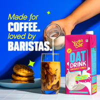Yoga Bar Unsweetened Oat Milk being poured into iced coffee next to a plate of waffles on a blue background.